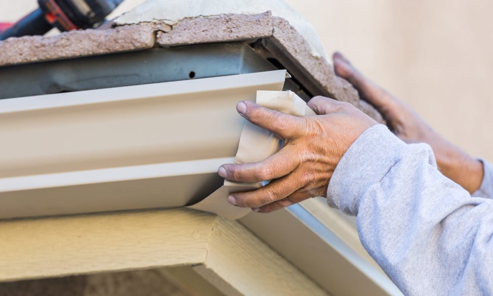 Worker Attaching Aluminum Rain Gutter to Fascia of House.